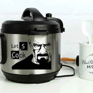 May include: A stainless steel electric pressure cooker with a black lid and handle. A black and white image of a man with a mustache and glasses is on the front of the cooker. The text "Let's Cook" is written below the image. The text "S" is in a box with the number "16" below it. The text "Cook" is in a box with the number "27" below it.
