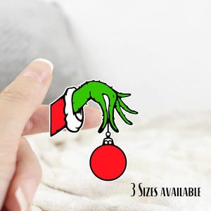 May include: A sticker featuring a green hand with long fingers, wearing a red and white Santa suit sleeve, holding a red Christmas ornament. The text "3 Sizes Available" is at the bottom.