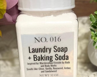 May include: A white plastic jar with a white lid containing laundry soap and baking soda. The label reads "NO. 016 Laundry Soap + Baking Soda Inspired by: Marshmallow Fireside by Bath and Body Works Smells like: Clove, Vanilla, Rosewood, Amber, and Sandalwood NT WT 32 OZ".