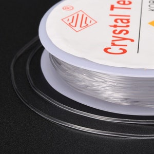 May include: A spool of clear elastic string for jewelry making. The spool is labeled "Crystal  Thread" and has a logo with a stylized "S" inside a diamond.