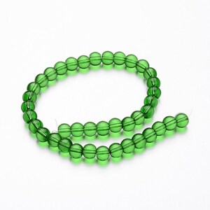 May include: A strand of green glass beads. The beads are round and have a slightly faceted appearance.
