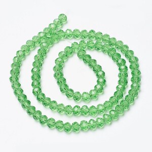 May include: A strand of light green faceted glass beads. The beads are round and have a shiny finish.