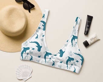 Puede incluir: Top de bikini blanco con estampado de tiburones azules. El top tiene un escote redondo y tirantes ajustables.