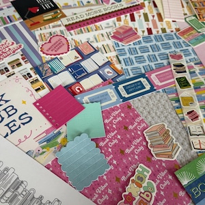 May include: A collection of book-themed stationery items including patterned paper, stickers, and cards. Features include a book tracker sheet, a pink 'Book Vibes Only' paper, a strip of book stickers, and text reading 'Book Club Rules' and 'Read More Books'.