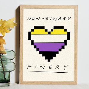 May include: A framed print with a pixelated heart in the non-binary pride flag colors: yellow, white, purple, and black. The words "NON-BINARY" and "FINERY" are written above and below the heart in a handwritten font.