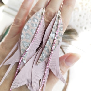 May include: A pair of pink feather earrings with a silver and pink leopard print design. The earrings have pink crystal accents and dangle from silver hooks.