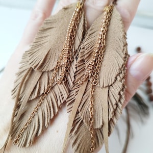 以下が含まれることがあります： ゴールドのチェーンとラインストーンが付いた、長い茶色の革の羽根のイヤリングのペア