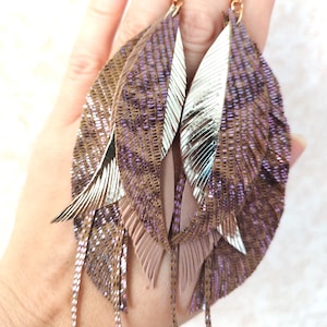 Puede incluir: Un par de pendientes largos de plumas marrones y plateadas. Las plumas están superpuestas y tienen un acabado brillante.