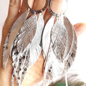 Puede incluir: Pendientes de plata con múltiples colgantes en forma de plumas. Las plumas son texturizadas y tienen un acabado metálico.