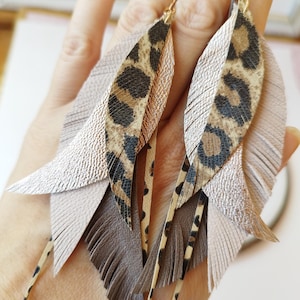 Peut inclure: Une paire de boucles d'oreilles pendantes avec un motif de plumes superposées. Les boucles d'oreilles sont dotées de crochets dorés, avec des couches de matériaux de couleur beige, marron et imprimé léopard. Les boucles d'oreilles sont conçues pour ressembler à des plumes.