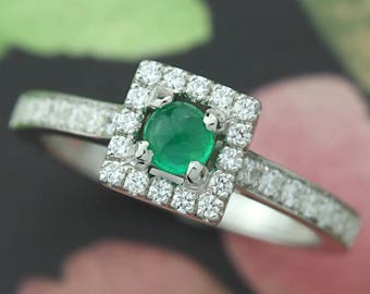 May include: A silver ring with a square emerald gemstone surrounded by a halo of smaller diamonds. The band is also set with smaller diamonds.