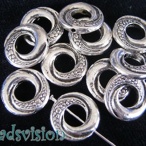 Könnte beinhalten: Eine Gruppe silberfarbener Metallringe mit einem Spiraldesign. Die Ringe haben einen Durchmesser von etwa 2,5 cm und ein Loch in der Mitte.
