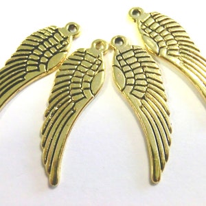 Könnte beinhalten: Vier goldfarbene Metall-Engel Flügel Charms mit einer strukturierten Oberfläche. Die Flügel sind mit Linien verziert und haben eine Schlaufe oben zum Anbringen an Schmuck oder andere Bastelarbeiten.