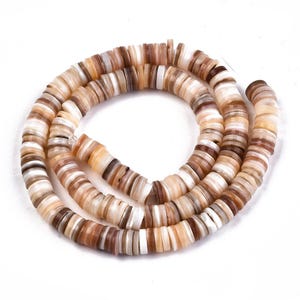 Könnte beinhalten: Eine Kette aus flachen, runden Perlen in verschiedenen Braun-, Beige- und Weißtönen. Die Perlen sind aufgefädelt und bilden eine Halskette oder ein Armband. Die natürliche Farbpalette deutet auf eine Verbindung zur Natur und Erdtöne hin.