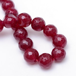 May include: A strand of deep red faceted gemstone beads. The beads are round and have a smooth, polished finish.