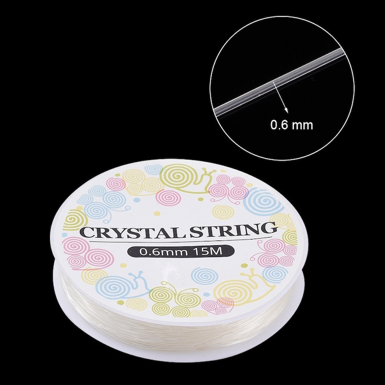 Peut inclure: Une bobine de fil de cristal transparent, de 0,6 mm d'&eacute;paisseur et de 15 m&egrave;tres de long, est pr&eacute;sent&eacute;e sur fond noir. L'&eacute;tiquette indique "CRYSTAL STRING" avec un motif tourbillonnant d&eacute;coratif.