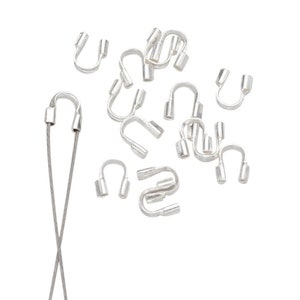 Könnte beinhalten: Nahaufnahme von silberfarbenen Metall-Quetschperlen und zwei silberfarbenen Metallschnüren. Die Quetschperlen befinden sich in verschiedenen Positionen, einige sind offen und einige sind geschlossen.