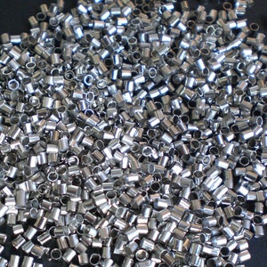 Könnte beinhalten: Ein großer Haufen silberfarbener Metall-Quetschperlen. Die Perlen sind klein und rund, mit einem Loch in der Mitte. Sie werden für die Schmuckherstellung verwendet.