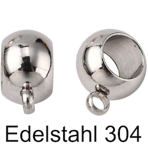 Könnte beinhalten: Zwei silberne Metallperlenkappen mit einer Schlaufe an der Unterseite. Die Perlenkappen sind rund und haben ein Loch in der Mitte. Der Text "Edelstahl 304" ist unter den Perlenkappen gedruckt.