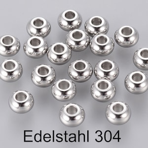 Könnte beinhalten: Eine Gruppe von 20 silbernen Metallperlen mit runder Form und einem Loch in der Mitte. Die Perlen sind auf einer grauen Oberfläche verstreut. Der Text "Edelstahl 304" ist unter den Perlen geschrieben.