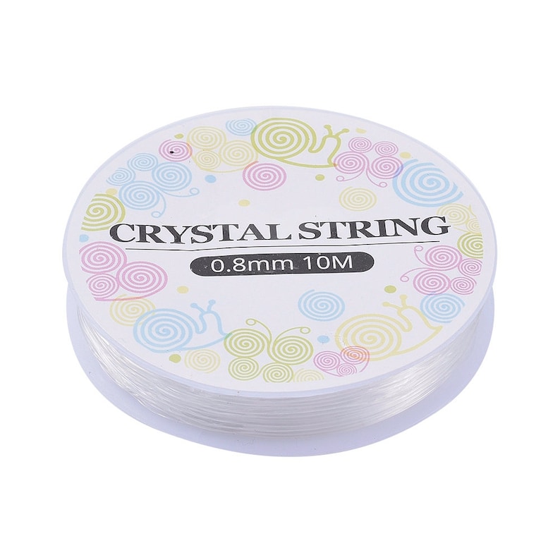 Peut inclure: Bobine de fil de cristal transparent, 0,8 mm d'&eacute;paisseur et 10 m&egrave;tres de long. L'&eacute;tiquette porte l'inscription "CRYSTAL STRING" avec des motifs de spirales et d'escargots aux couleurs pastel. Le fil est bien enroul&eacute;.