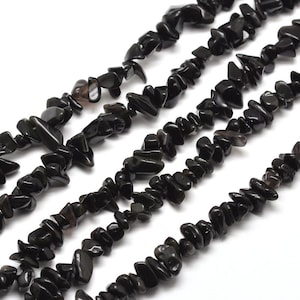 Könnte beinhalten: Nahaufnahme von mehreren Strängen schwarzer Obsidian-Chip-Perlen. Die Perlen sind unregelmäßig geformt und haben eine polierte, reflektierende Oberfläche. Der Hintergrund ist weiß und hebt die dunkle Farbe und Textur der Perlen hervor.