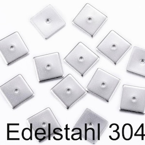 May include: Ten silver square metal beads with a hole in the centre. The beads are scattered on a white surface. The text "Edelstahl 304" is printed below the beads.