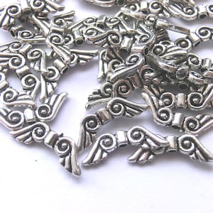 Könnte beinhalten: Ein Haufen silberner Engelsflügel-Anhänger aus Metall mit filigranen Details. Die Anhänger sind perfekt für die Schmuckherstellung, das Scrapbooking und andere Bastelprojekte.