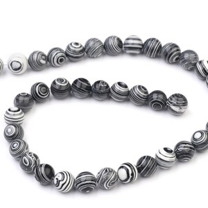 Könnte beinhalten: Eine Kette aus schwarzen und weißen, gestreiften runden Perlen. Die Perlen sind aus einem Naturstein mit einem wirbelnden Muster.