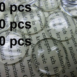 Könnte beinhalten: Nahaufnahme eines Stapels klarer Glascabochons oder runder Glaskuppeln auf einer bedruckten Seite. Der Text auf der Seite ist durch das Glas sichtbar. Das Bild enthält den Text "10 pcs", "20 pcs" und "50 pcs".