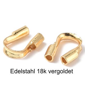 Könnte beinhalten: Zwei goldfarbene, U-förmige Schmuckverschlüsse. Jeder Verschluss hat ein zylindrisches Ende und einen gebogenen, offenen Abschnitt. Der Text "Edelstahl 18k vergoldet" ist darunter gedruckt.