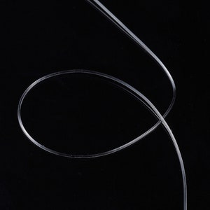 Peut inclure: Un filament de plastique clair, fin et flexible, possiblement un c&acirc;ble &agrave; fibre optique, se courbe et se croise sur un fond noir. Le mat&eacute;riau semble lisse et r&eacute;fl&eacute;chissant, avec des reflets subtils.