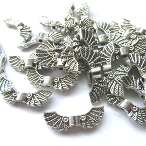 Könnte beinhalten: Eine Gruppe von silbernen Flügel-Anhängern aus Metall mit einem detaillierten Design. Die Anhänger liegen auf einer weißen Oberfläche.
