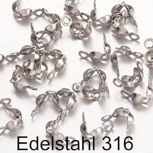 Può includere: Primo piano di un gruppo di cappucci per perline in metallo color argento. I cappucci sono progettati per la creazione di gioielli e hanno un piccolo anello su un'estremità. Il testo "Edelstahl 316" è visibile nell'immagine.