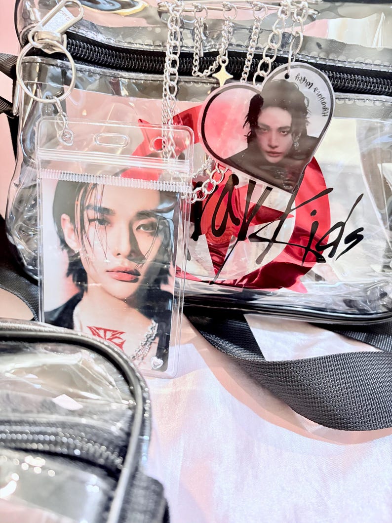 Puede incluir: Una bolsa de pl&aacute;stico transparente con una correa negra y una cadena plateada. La bolsa tiene un dije en forma de coraz&oacute;n rojo con una foto de una persona dentro. La bolsa tambi&eacute;n tiene un bolsillo de pl&aacute;stico transparente con una foto de una persona dentro. La bolsa tiene las palabras "Stray Kids" escritas en ella.