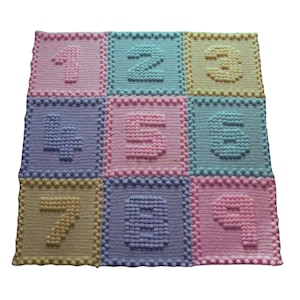 May include: A crocheted baby blanket featuring the numbers 1 to 9 in a colourful pattern of pink, yellow, blue and purple.