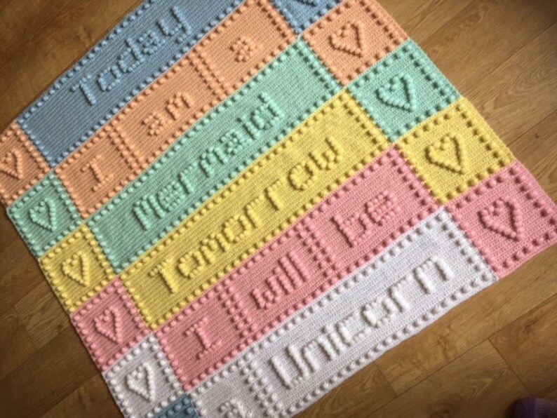 May include: A colorful crocheted baby blanket with a rainbow of colors and the words "Today I am", "Not ready", "Tomorrow", "I will be", and "Unicorn" in raised lettering.