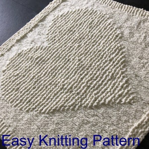 May include: A white knitted blanket with a heart-shaped design. The blanket is made with a textured stitch that creates a raised effect. The text "Easy Knitting Pattern" is visible at the bottom of the image.