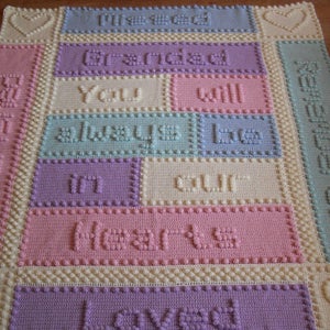 May include: A crocheted baby blanket in pastel colours. The blanket features a heart design and the text "You will always be in our hearts."