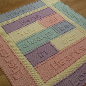 May include: A crocheted baby blanket with a pastel colour scheme. The blanket features the words "You will always be in our hearts" in a variety of colours.