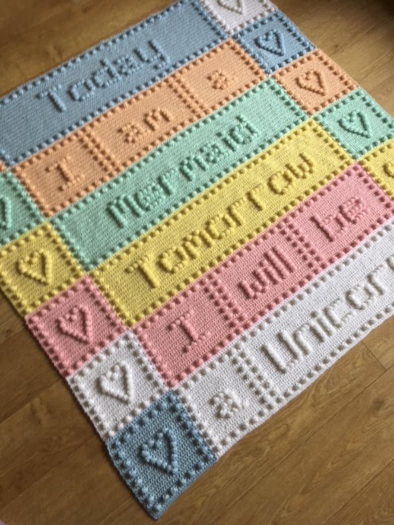 May include: A multi-colored crocheted baby blanket with the words "Today I am", "Tomorrow I will be", and "A Unicorn" in white.