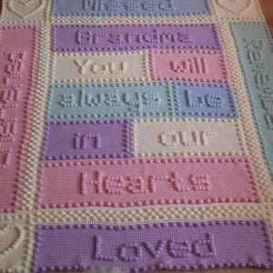 May include: A crocheted baby blanket in pastel colours. The blanket features a heart design and the words "You will always be in our hearts loved".