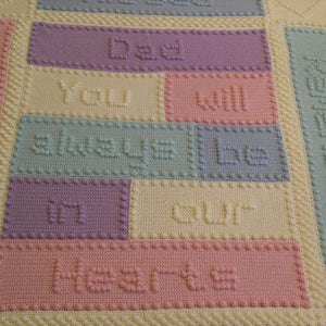 May include: A crocheted baby blanket in pastel colours. The blanket features the words "You will always be in our hearts" in a colourful block pattern.