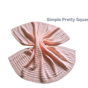 A soft pink knitted baby blanket with a simple square pattern. The blanket is folded and draped over itself, showing the texture of the knit.