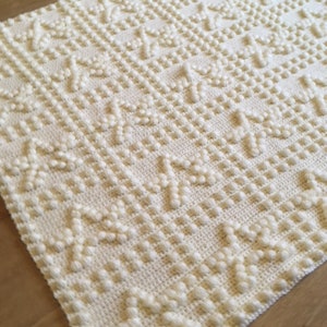May include: A white crocheted baby blanket with a textured pattern of raised dots.