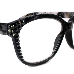 May include: Black cat-eye glasses with a marble pattern on the arms and rhinestones on the frame.