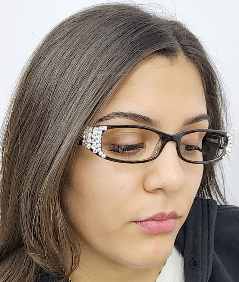 May include: A woman wearing black framed glasses with rhinestones on the temples. The glasses have a cat-eye shape.
