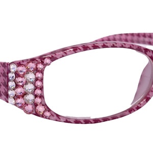 May include: Pink eyeglasses with a houndstooth pattern and clear lenses. The frames are decorated with a row of clear rhinestones.