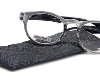 Puede incluir: Gafas de lectura grises con patillas de muelle y una funda negra. Las gafas tienen un acabado moteado y una graduación de +2,25.