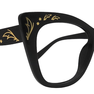 May include: Black cat-eye glasses with gold leaf and star accents. The frames have a classic shape with a modern twist, featuring decorative gold detailing on the arms and upper rims. A stylish accessory for vision correction or fashion.